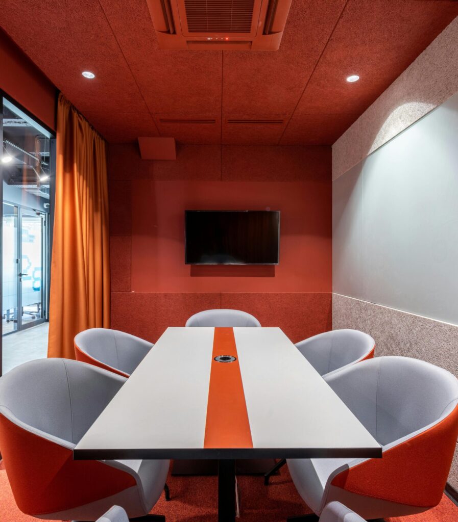 Comfortable chairs at tale placed against red wall with TV in modern conference room with glass wall in business center